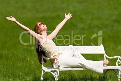 Red hair woman enjoying sun on white bench in spring
