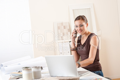 Young female designer on the phone at office with laptop