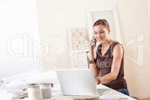 Young female designer on the phone at office with laptop