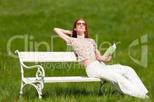 Red hair woman sitting in spring on white bench in spring