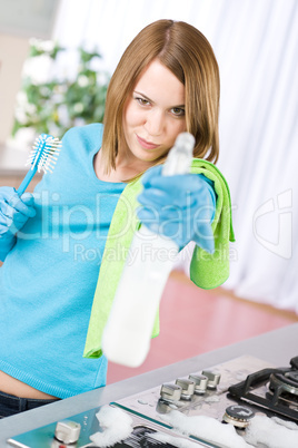 Woman cleaning stove with spray in kitchen