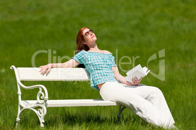 Red hair woman with book enjoying sun on white bench in spring