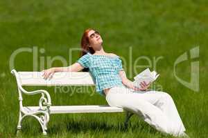 Red hair woman with book enjoying sun on white bench in spring