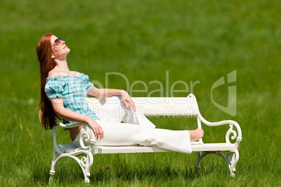 Red hair woman enjoying sun on white bench in spring