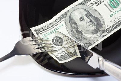 Banknote on a black plate with knife and fork