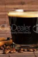 espresso in einem kleinen glas neben zimt und kaffeebohnen