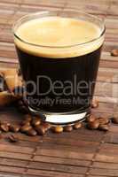 espresso in einem kleinen glas neben zimtstangen und kaffeebohnen