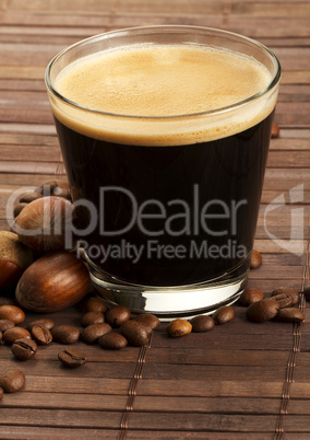 espresso in kleinem glas daneben haselnüsse und kaffeebohnen