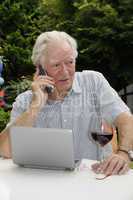Rentner mit Handy, Netbook und Rotwein