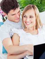 young couple sitting on a sofa using laptop