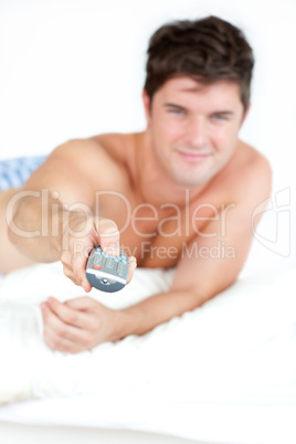 man with pyjamas using a remote lying on his bed