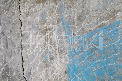Hellgraue Betonmauer mit Riss und Fissuren sowie türkisblauem Restfarbanstrich