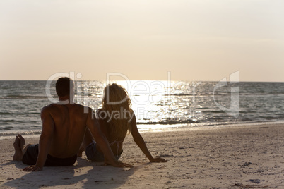 Young Man and Woman Couple Sitting on Beach At Sunset