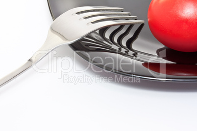 Red tomato on a black plate with fork