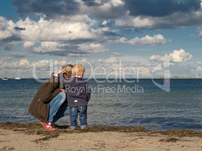 Mother and child at a beach looking towards the sea in autumn