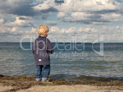 Little boy at a beach looking towards the sea in autumn