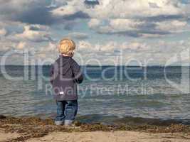 Little boy at a beach looking towards the sea in autumn