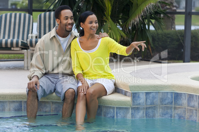 Happy African American Couple Sitting By Swimming Pool Pointing