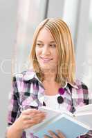 Happy young blond woman holding books