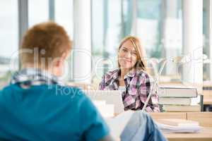 Two students with books and laptop in classroom