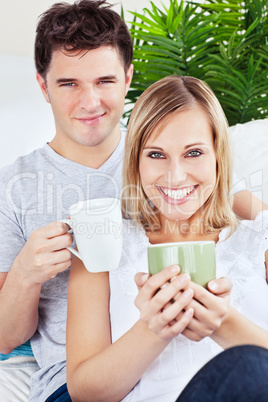 couple resting on the sofa and holding cups