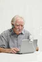 Älterer Herr mit Netbook, Webcam und Headset