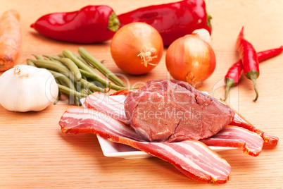 rohes Fleisch und Speckstreifen auf einem Holztisch