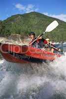 Two people paddling inflatable boat down rapids