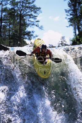 Young man kayaking down waterfall