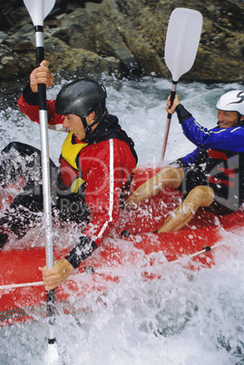 Two people paddling inflatable boat down rapids