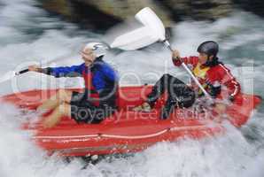 Two people paddling inflatable boat down rapids