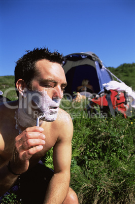 Man shaving in the outdoors next to tent