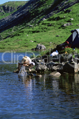 Young woman washing clothes in lake next to tent