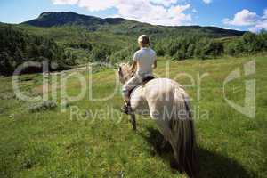 Rear view of young woman riding horse in rural setting