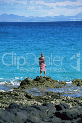 Young woman standing rocks, looking out to sea