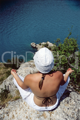 Young woman meditating on rocks at water's edge