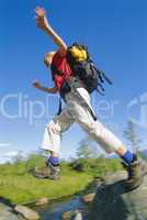 Young woman wearing backpack leaping across river