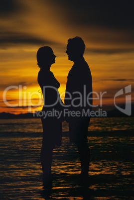 Silhouette of couple standing face to face on beach at sunset