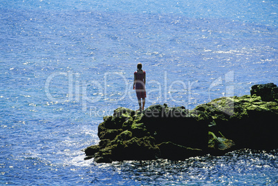 Young woman standing rocks, looking out to sea