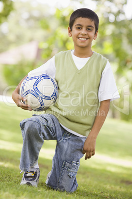 Ein Junge kniet lachend im Gras mit Fussball
