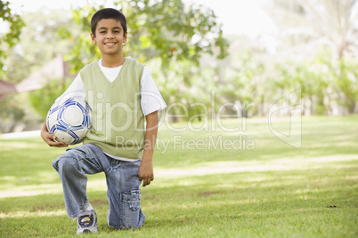 Ein Junge kniet lachend im Gras mit Fussball