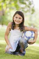 Ein junges  Mädchen kniet im Gras mit Fussball