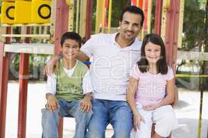 Vater sitzt mit seinen Kindern auf dem Spielplatz