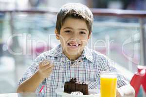 Young boy having orange juice and cake