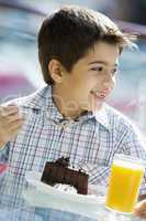 Young boy having orange juice and cake