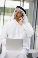 A Middle Eastern businessman using a mobile phone and laptop