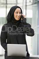 A Middle Eastern businesswoman using a laptop and a cellphone