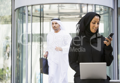 A Middle Eastern businesswoman using a laptop and a cellphone