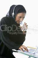 A Middle Eastern businesswoman using a laptop and phone headset