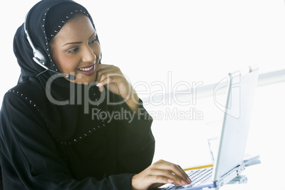 A Middle Eastern businesswoman using a laptop and phone headset